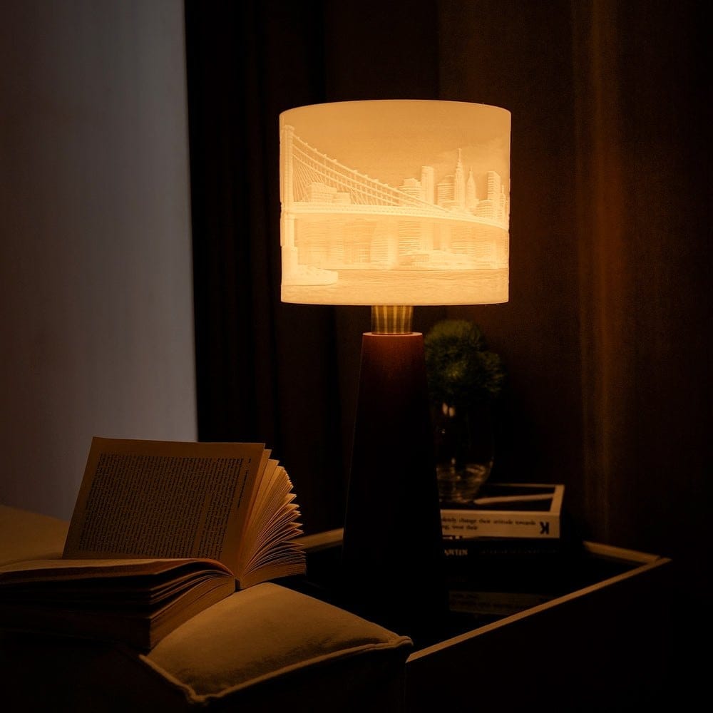A Drum photo lamp with a city skyline glowing in its shade, beside an open book