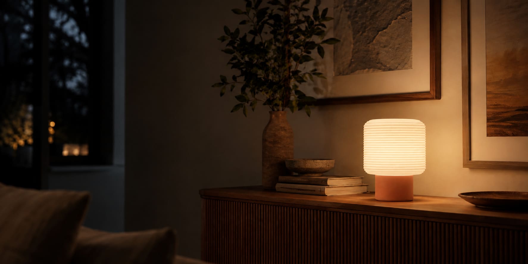 An OVLIGHT table lamp glowing on a sideboard in a dark room at dusk